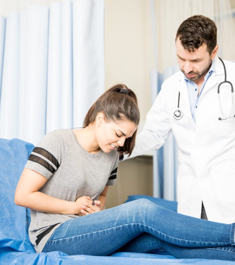 Beautiful young woman having severe stomach ache visiting doctor for treatment