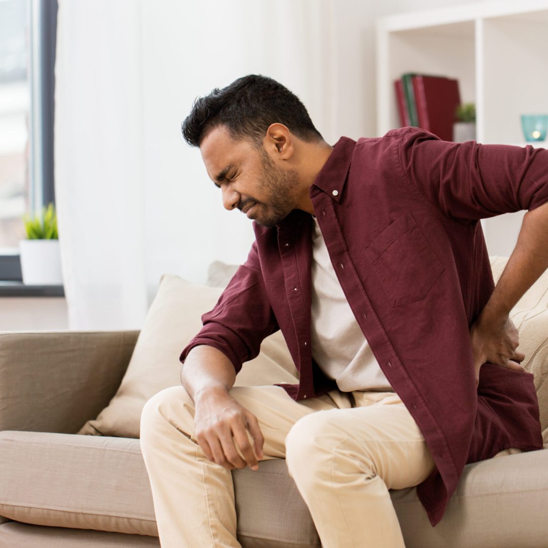 people, health care and problem concept - unhappy man suffering from pain in back or reins at home